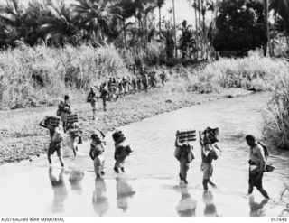 RAGITSUMA, NEW GUINEA, 1943-09-30. NATIVES CARRYING AMMUNITION AND SUPPLIES ACROSS THE YATI RIVER IN THE MARKHAM VALLEY