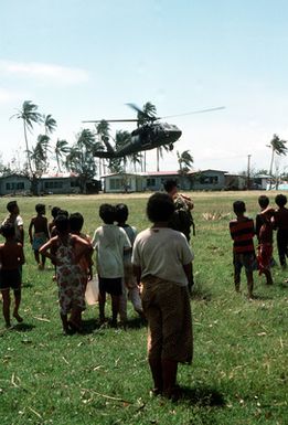 Villagers watch a 53rd Aviation Battalion UH-60 Black Hawk Helicopter as it prepares to land with a delivery of supplies. Military personnel from the United States and other nations are providing such services to the islands of Upolu and Savaii as part of disaster relief efforts in the aftermath of Cyclone Ofa