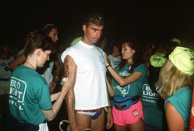 Race officials number the arms of LT Chris Lewis prior to start of the swimming event at the 1989 Ironman Triathlon. Lewis, a member of the 548th Reconnaissance Technical Group at Hickam Air Force Base, eventually placed 326th out of 1,246 participants in the race, which features a 2.4-mile swim, a 112-mile bicycle ride and a 26.2-mile marathon run