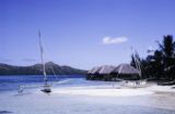 French Polynesia, outrigger canoe docked on beach near stilt homes in Bora Bora