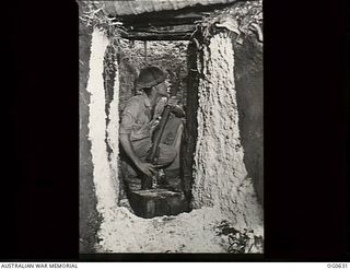 KIRIWINA, TROBRIAND ISLANDS, PAPUA. 1944-01-31. CORPORAL W. GORDON, MELBOURNE, VIC, RADIO OPERATOR, CROUCHES IN A SLIT TRENCH WITH RIFLE HANDY DURING AIR RAID ALERT AT NO. 79 (SPITFIRE) SQUADRON ..