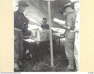 ALEXISHAFEN, NEW GUINEA. 1944-05-27. TROOPS FROM HEADQUARTERS 8TH INFANTRY BRIGADE OUTSIDE A TENT COVERED POLLING BOOTH TO RECORD THEIR VOTES IN THE NEW SOUTH WALES STATE ELECTIONS. IDENTIFIED ..