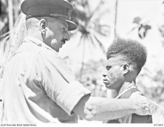 LAE, NEW GUINEA. 1944-04-01. MAJOR GENERAL B.M. MORRIS, DSO, (1), GENERAL OFFICER COMMANDING AUSTRALIAN NEW GUINEA ADMINISTRATIVE UNIT, PRESENTS CONSTABLE YARAWA (2), WITH THE LOYAL SERVICE MEDAL ..