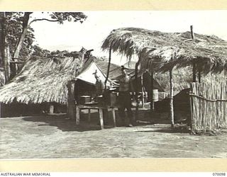 DUMPU, NEW GUINEA. 1944-01-25. VX11457 PRIVATE M. TAYLOR (1) AND QX31346 PRIVATE S.J. LEE (2) TWO COOKS OF "B" COMPANY 2/1ST GUARD REGIMENT PICTURED IN FRONT OF THE COMPANY COOKHOUSE