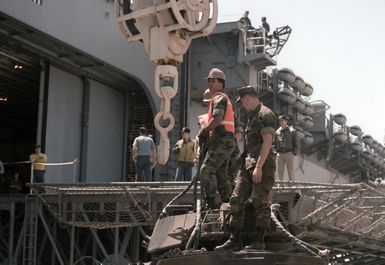 Crew members prepare to attach a hoist to an armored vehicle while loading the amphibious assault ship USS GUAM (LPH 9) during Exercise SOLID SHIELD '87