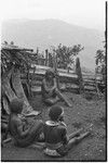 Bride price ritual: bride wearing large shell valuables sits with women and small children next to a house