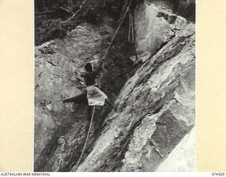 NEW GUINEA. 1944-07-09. A NEW GUINEA NATIVE, EMPLOYED BY THE ROYAL AUSTRALIAN ENGINEERS, CLIMBING A STEEP ROCK FACE DURING THE CONSTRUCTION OF THE WAU-BULLDOG ROAD