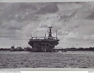 MANUS ISLAND, NEW GUINEA. 1949-09. STERN VIEW OF THE AIRCRAFT CARRIER HMAS SYDNEY (III) AT ANCHOR. NOTE THE TYPE 960 AIR SEARCH RADAR AT THE MASTHEAD, TYPE 293Q AIR/SURFACE SEARCH RADAR JUST BELOW ..