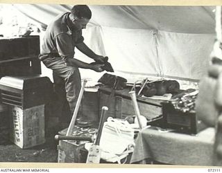 LAKONA, NEW GUINEA. 1944-04-05. NX114181 CAPTAIN A.E. RICKARDS, THE AMENITIES OFFICER AT HEADQUARTERS 5TH DIVISION, CHECKING SPORTING GEAR AND EQUIPMENT PROVIDED BY THE ARMY AMENITIES SERVICE PRIOR ..