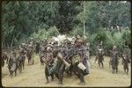 Pig festival, singsing, Kompiai: decorated men dance and play drums, observed by children