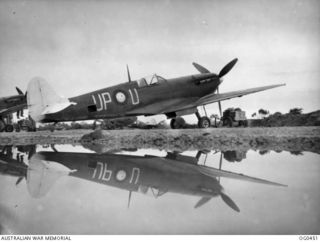 KIRIWINA, TROBRIAND ISLANDS, PAPUA. 1944-01-11. THE SPITFIRE AIRCRAFT SPEED THROUGH HEAVY RAIN UP NORTH. A POOL LEFT BY A TROPICAL DOWNPOUR REFLECTS PERFECTLY THE BEAUTIFUL LINES OF A SPITFIRE ..