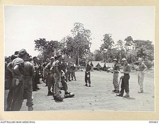 NANTAMBU, NEW BRITAIN, 1945-08-22. MEMBERS OF A COMPANY, 37/52ND INFANTRY BATTALION AT THEIR FINAL MESS PARADE IN THE STAGING AREA BEING WARNED FOR PLANE DRAFT BY CAPTAIN G.R. WEST, COMPANY ..