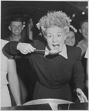 Betty Hutton visits chow halls with sailors and Marines in the Marshall Islands. Peering over the screen star's shoulder is Virginia Carrol, dancer with the Hutton troupe.