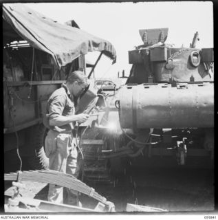 CAPE WOM, WEWAK AREA, NEW GUINEA. 1945-08-30. CORPORAL R.G. HUGGINS, 2/4 ARMOURED REGIMENT WORKSHOP, CORPS OF AUSTRALIAN ELECTRICAL AND MECHANICAL ENGINEERS, USING AN ELECTRIC WELDER ON A MATILDA ..