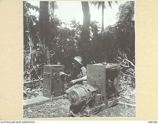 SEKULA RIVER AREA, NEW GUINEA. 1944-07-10. A MEMBER OF THE 5TH DIVISION CARRIER COMPANY, 5TH DIVISION SALVAGE GROUP, ALONGSIDE A JAPANESE GENERATOR USED TO SUPPLY POWER TO HIS UNIT