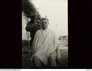 ALEXISHAFEN, NEW GUINEA. 1944-06-10. VX72574 LANCE CORPORAL A. D. MCNICOLL (LEFT) GIVES A HAIRCUT TO QX27426 PRIVATE J. W. BONDING IN FRONT OF THE MAIN DRESSING STATION OF 2/15TH FIELD AMBULANCE