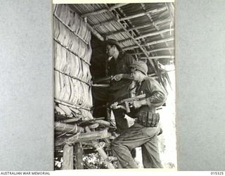 1943-07-29. ALLIED CAPTURE OF MUBO. WITH THEIR FINGERS ON THE TRIGGER OF A RIFLE AND LIGHT AUTOMATIC, CPL. MAX HAMILTON OF MELBOURNE AND SGT. JIM GARRICK OF NEWBURG, OREGON, EXAMINE A HUT IN A ..