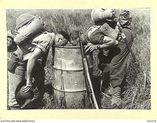 DUMPU, NEW GUINEA. 1944-01-03. VX82161 PRIVATE M. V. CAREY (1) AND PRIVATE F. CAULFIELD (2) OF THE 2/12TH INFANTRY BATTALION, 18TH INFANTRY BRIGADE, QUENCHING THEIR THIRST FROM A DRUM OF DRINKING ..