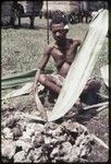 Woman heats and flattens pandanus leaf over a fire, softening it for use in weaving