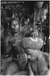 Pig festival, wig ritual, Tsembaga: man applies painted design to red wig