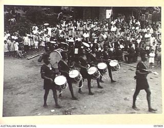 RATONGOR, NEW BRITAIN. 1945-10-10. ANERILA, THE SOLDIER LIKE DRUM MAJOR OF THE ROYAL PAPUAN CONSTABULARY BAND, LEADS A QUINTET OF DRUMS TO THE DELIGHT OF THE CHINESE CHILDREN. THEY ARE ATTENDING ..