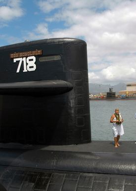 Brother Franklin Pao stands next to the sail of the Los Angeles Class Attack Submarine USS HONOLULU (SSN 718) as he performs the Hawaiian water blessing during a farewell ceremony, at Pearl Harbor, Hawaii (HI)