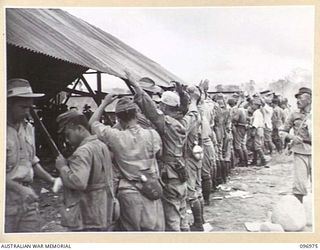 TOROKINA, BOUGAINVILLE. 1945-09-23. OFFICERS OF 9 INFANTRY BATTALION, WHO CONTROL THE CHOP CHOP TRAIL CONCENTRATION CAMP, CARRYING OUT A PERSONAL SEARCH OF JAPANESE NAVAL TROOPS IN THE SEARCHING ..