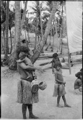 Woman wearing a grass skirt holding an infant and two baskets, Port Moresby, Papua, ca. 1923, 2 / Sarah Chinnery