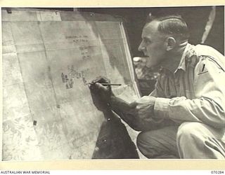 DUMPU, RAMU VALLEY, NEW GUINEA, 1944-02-11. NX51600 LIEUTENANT A.P. HAMILTON, INTELLIGENCE OFFICER OF THE 57/60TH INFANTRY BATTALION MARKING THE BATTALION LOCATION MAP