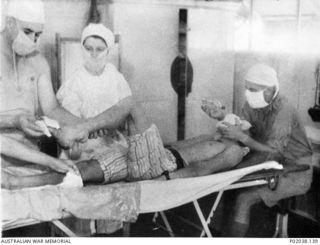 Port Moresby, Papua. 1941-12. A patient on the operating table in No. 5 Casualty Clearing Station. The soldier had been bayoneted during combat on the Kokoda Track. An anaesthetist, nursing sister ..