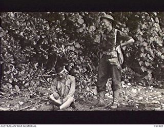 FINSCHHAFEN, NEW GUINEA. 1943-09-22. NX29349 CORPORAL J. RICHMOND, AUSTRALIAN PROVOST CORPS, FINSCHHAFEN FORCE STANDS GUARD OVER A CAPTURED JAPANESE SOLDIER