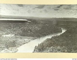 An aerial view of Upoia village and camp on the bank of a creek from the Junkers seaplane used for carrying equipment and mail to remote regions. Portion of the aircraft's tailplane can be seen at ..