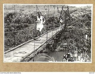 DONADABU, PAPUA, NEW GUINEA. 1944-01-01. PRIVATE N. E. PLANT CROSSING A NARROW BRIDGE DURING THE RUNNING OF THE 3000 YARDS CROSS COUNTRY RACE AT THE 15TH INFANTRY BRIGADE GYMKHANA