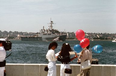 Spectators stand by on the pier as a commercial harbor tug maneuvers the miscellaneous flagship USS CORONADO (AGF-11)into port at Naval Air Station, North Island, San Diego. The CORONADO, flagship for Commander, Third Fleet, will be arriving at its new home port after being stationed in Hawaii for almost 20 years