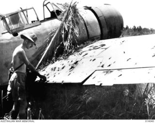 1943-01-08. PAPUA. BUNA. CAPTURED AIR STRIP AT BUNA. JAPANESE LEFT BEHIND PLANES STRAFED BY ALLIED FIGHTERS. NOTE BULLET HOLES IN WING OF ZERO. THIS IS ONE OF THE NEW TYPE SQUARE WING ZERO AIRCRAFT