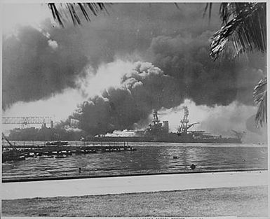 Naval photograph documenting the Japanese attack on Pearl Harbor, Hawaii which initiated US participation in World War II. Navy's caption: The smoldering battleship USS NEVEDA silhouetted in the fire and smoke of the destroyer USS SHAW which exploded when her magazine was hit by bombs from Japanese aircraft during the attack on Pearl Harbor on Dec. 7, 1941.