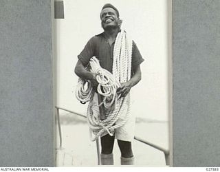 CLIFTON GARDENS, SYDNEY, AUSTRALIA. 1942-12. A NATIVE OF THE PACIFIC ISLANDS IN HAPPY MOOD AS HE TAKES CORDAGE ABOARD ONE OF THE SHIPS OPERATED BY 1 AUSTRALIAN WATER TRANSPORT GROUP WITH WHICH HE ..