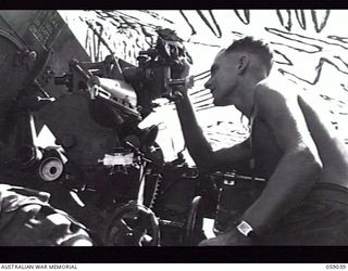 RAMU VALLEY, NEW GUINEA. 1943-10-23. VX21695 BOMBARDIER G. D. O'NEILL LAYING A GUN OF THE 54TH BATTERY, 2/4TH AUSTRALIAN FIELD REGIMENT UNDER CAMOUFLAGE