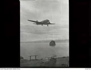 LAE, NEW GUINEA. C. 1944-02. A DOUGLAS TRANSPORT AIRCRAFT COMING IN TO LAND ON LAE AIRSTRIP OVER THE TOP OF A DAMAGED HALF-SUBMERGED JAPANESE SHIP, TENYO MARU, THAT WAS BOMBED BY RAAF AIRCRAFT AND ..