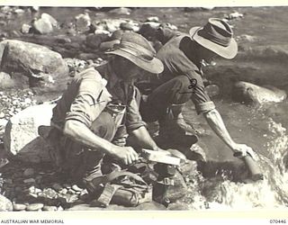 FARIA RIVER, NEW GUINEA, 1944-02-15. VX122642 PRIVATE S.I. RAWLING (1) WITH VX147260 PRIVATE Z.E. ROBERTS (2) MEMBERS OF NO.14 PLATOON, "C" COMPANY, 57/60TH INFANTRY BATTALION, FILL THEIR WATER ..