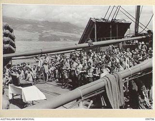 AT SEA, CAIRNS-MOROTAI. 1945-04-15. TROOPS OF HEADQUARTERS 9 DIVISION ATTENDING THE PROTESTANT CHURCH PARADE ON NO. 3 HATCH, WITH THE NEW GUINEA COAST BETWEEN SIO AND SAIDOR IN THE BACKGROUND. THE ..