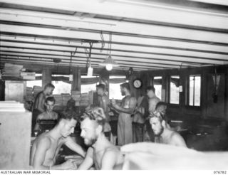 MADANG, NEW GUINEA. 1944-10-31. MEMBERS OF THE RAN ADMINISTRATION STAFF AT WORK ABOARD THE HMAS PING WO AN OLD CHINESE RIVER STEAMER WHICH HAS BEEN CONVERTED INTO AN OFFICE FOR THE UNIT