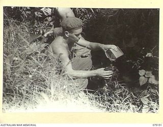 BOUGAINVILLE ISLAND. 1945-02-17. NX152906 PRIVATE R. SMITH, 9TH INFANTRY BATTALION FILLING HIS WATER BOTTLE FROM A MOUNTAIN STREAM NEAR MOSIGETTA