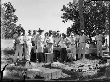 [Full-length group portrait of men standing around a table outdoors]