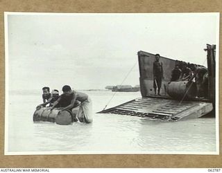 SIALUM BEACH, NEW GUINEA. 1944-01-08. NATIVES UNLOADING 44 GALLON DRUMS OF PETROL AND OIL FROM AN LCM (LANDING CRAFT MECHANISED)