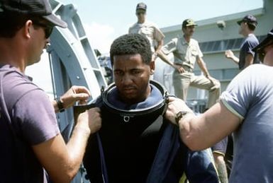 A member of Mobile Diving Salvage Unit 1 is helped with his diving suit before making a dive. Salvage Unit 1 is participating in the joint Navy/Park Service project SeaMark, a surveying and charting effort to assess submerged cultural resources in the Pacific