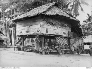 BUKAWA, HUON GULF, NEW GUINEA. 1944-12-14. THE YOUNG MEN OF A VILLAGE EAST OF LAE VISITED BY 43 LANDING CRAFT COMPANY MEMBERS SLEEP IN THIS HUT. THE PAINTINGS AND CARVINGS ON THE SIDE OF THE HUT ..