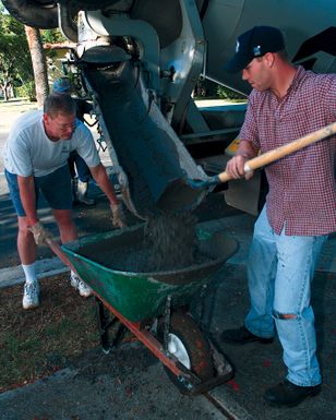 US Air Force SENIOR AIRMAN Brian Lawrence from the 15th Civil Engineering Squadron, Hickam Air Force Base, Hawaii, pours concrete in a wheelbarrow that USAF Colonel Joe Dent, from the legal office, will haul away while participating in the Families Helping Families program