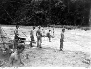 LAE, NEW GUINEA. 1944-08-08. TROOPS OF THE 20TH FIELD COMPANY, USING THEIR "FLYING FOX" TO GET TIMBER ACROSS THE RIVER DURING THE CONSTRUCTION OF A NEW BRIDGE. OVERHEAD CAN BE SEEN THE PIPES ..