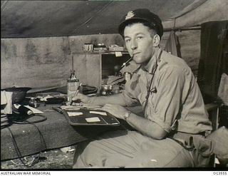 VIVIGANI, GOODENOUGH ISLAND, PAPUA. 1943-11. 401751 FLYING OFFICER (FO) ARCH W. MOORE OF BENDIGO, VIC, A PILOT OF NO. 79 (SPITFIRE) SQUADRON RAAF, AT HIS DESK. ON 1943-11-28, FO MOORE WAS ON A TEST ..